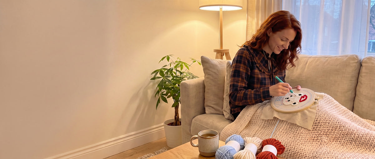 Une femme pique un kit punch needle ours polaire sur son canapé, plaid et tisane